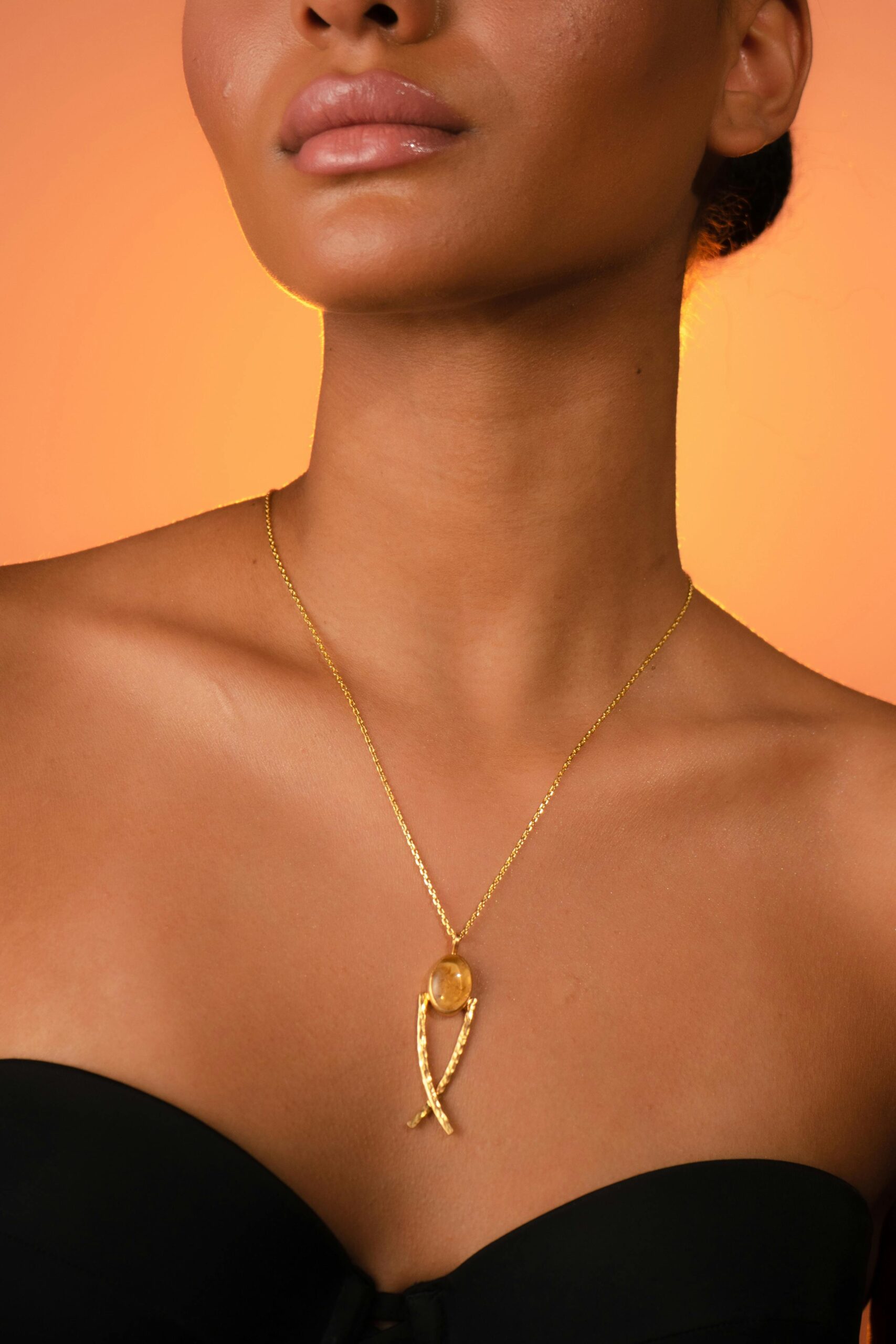 Close-up of a woman showcasing an elegant golden necklace against a warm background.