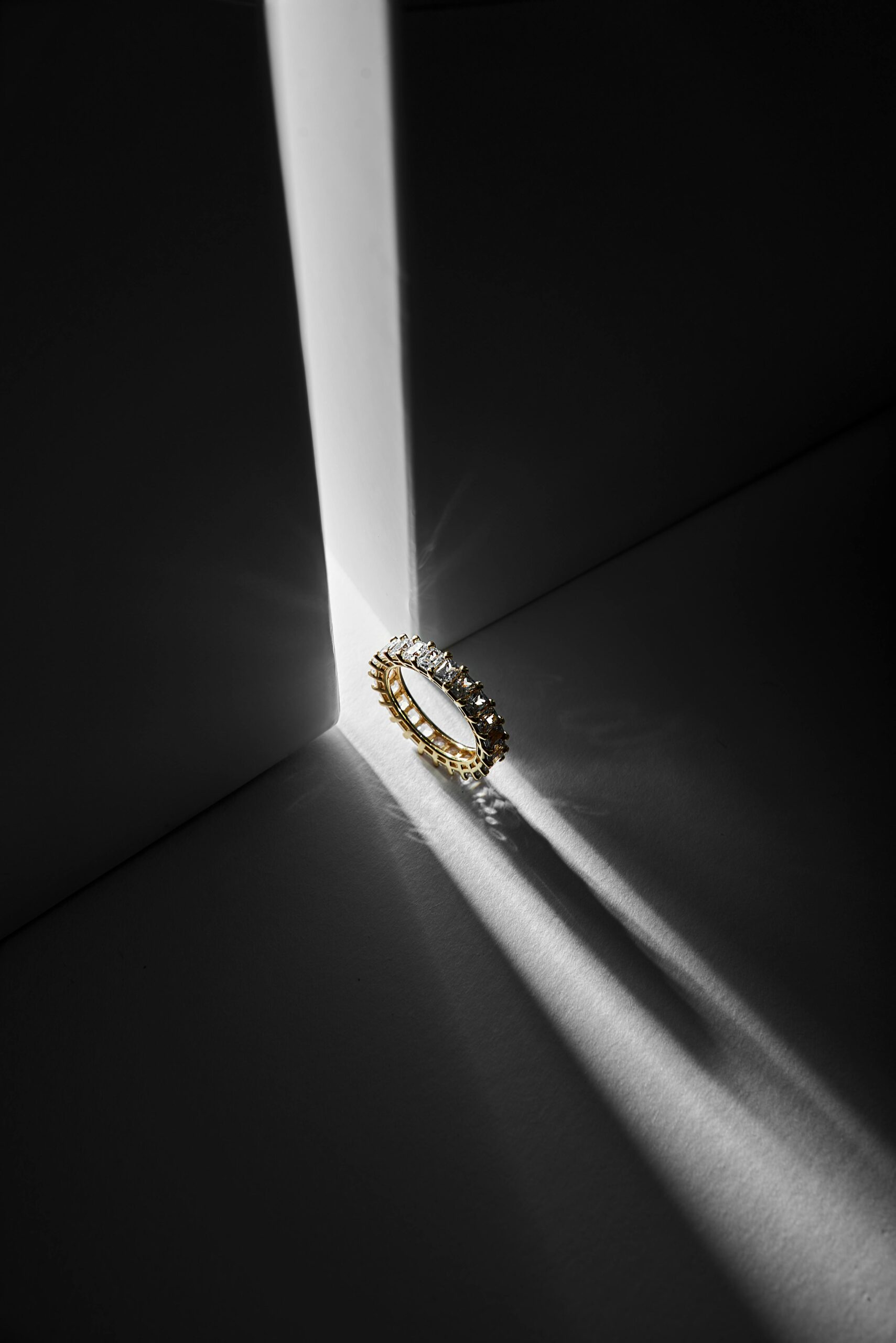 Luxury diamond and gold ring highlighted by striking shadows in a minimalist setting.